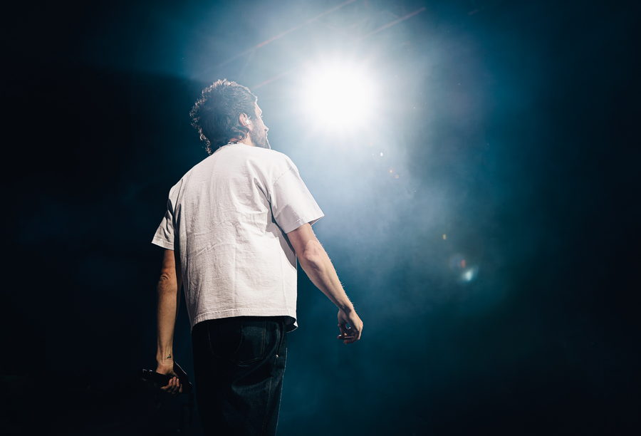 Kasabian's singer from behind, facing a single hard spotlight burning through the haze