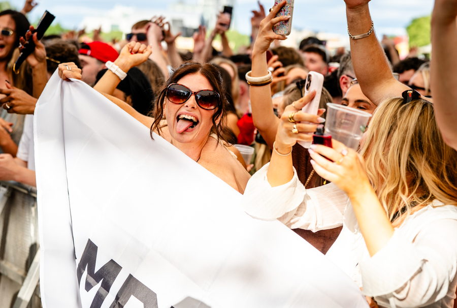 A fan at the front barrier holding a white flag wide open, arms raised among phones and drinks