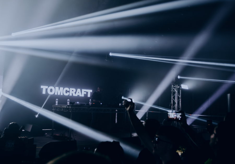 Tomcraft behind the decks under crossed white beams, hands and phones raised in the foreground