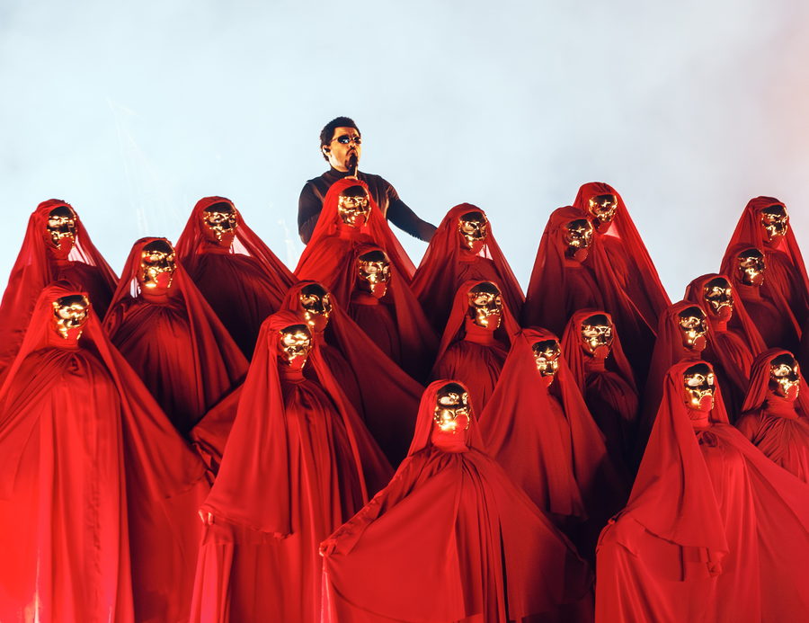 The Weeknd standing above a crowd of performers in red hooded robes filling the stage